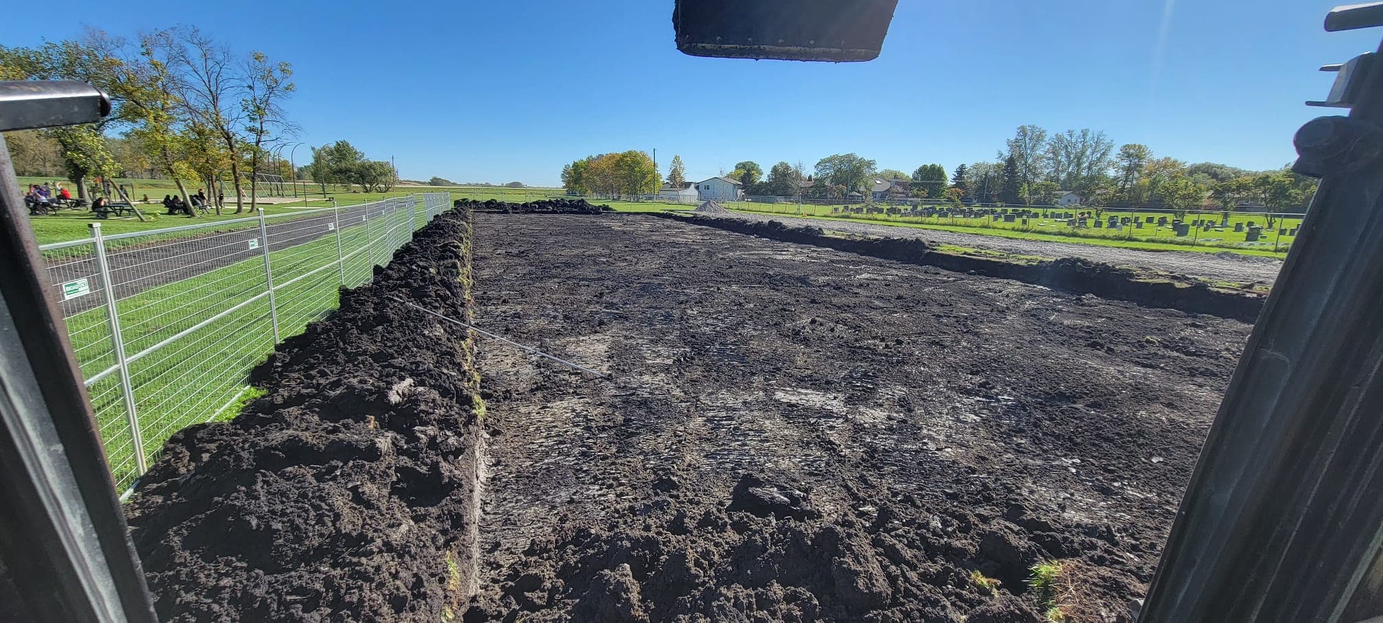 Rectangular plot of dark, excavated soil at a construction site, viewed from heavy machinery.