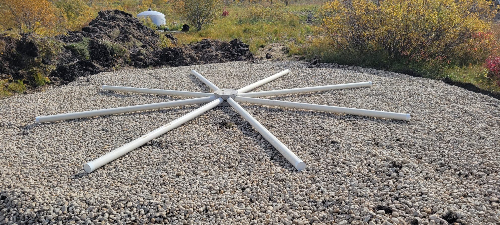 Starburst arrangement of white PVC pipes on a circular bed of grey gravel.