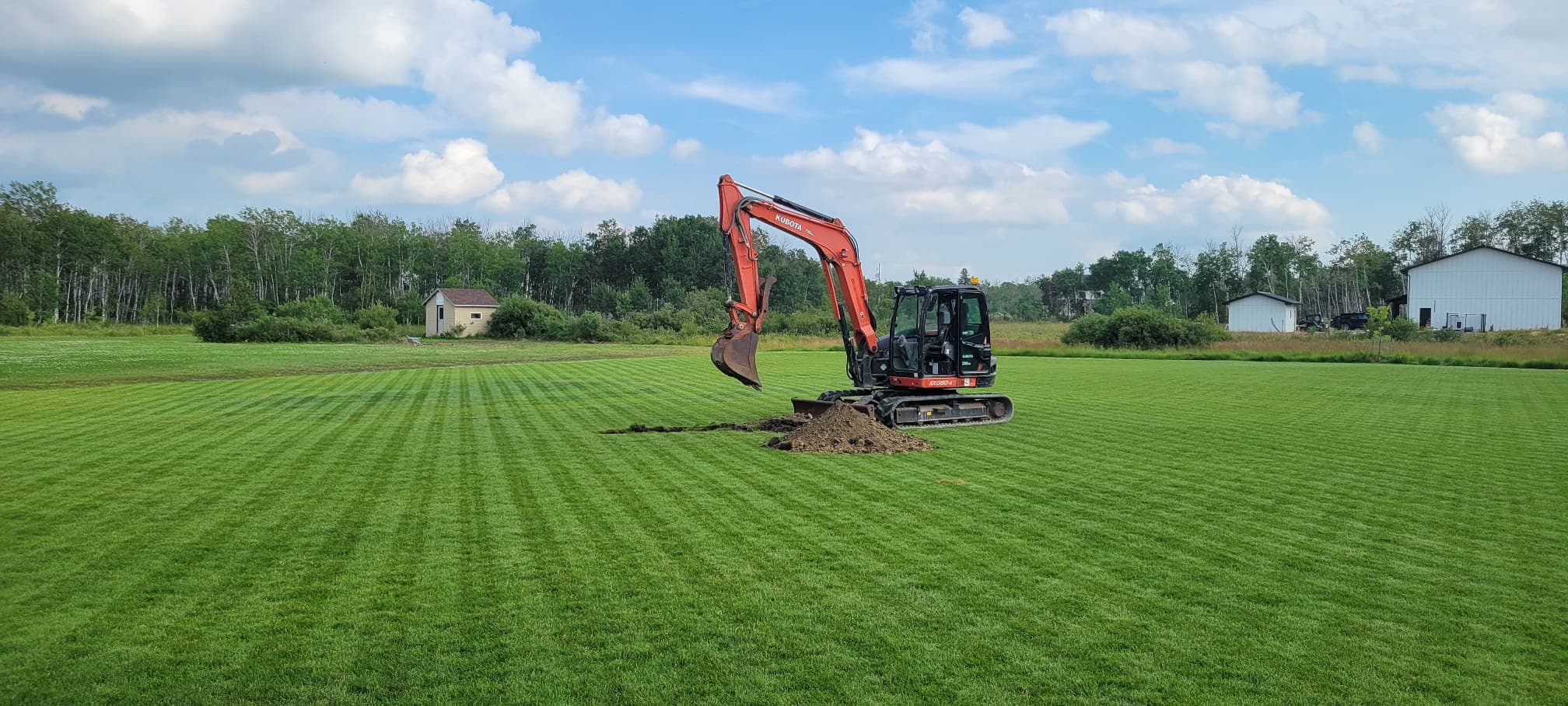 Orange excavator digging a hole in a large, manicured green field with a forest background.